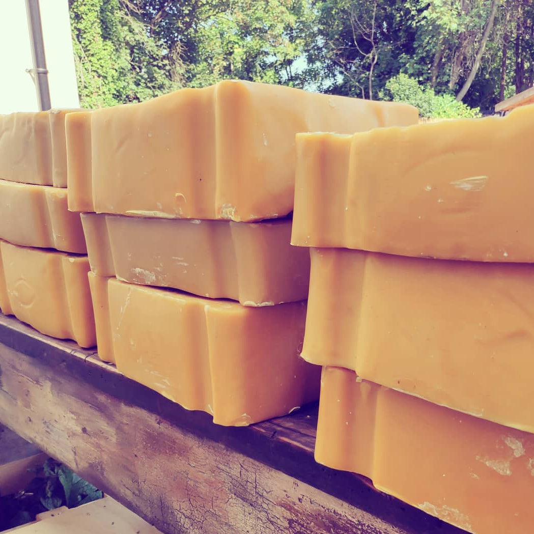 Stacks of rectangular blocks of african 1kg beeswax. warm golden-yellow color, arranged on a rustic wooden table outdoors with trees in the background.