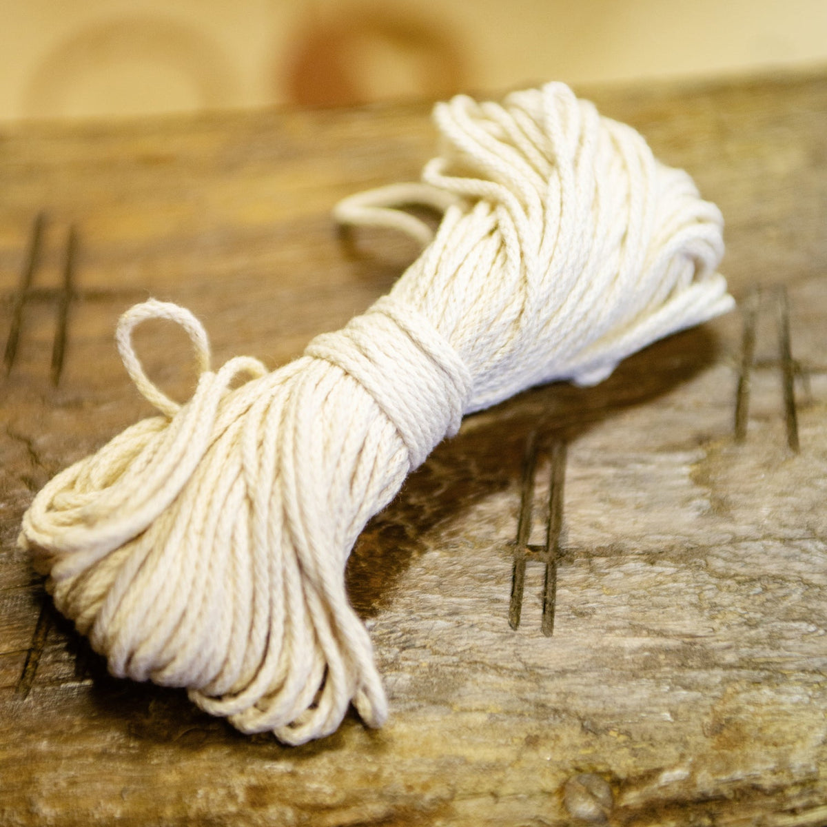 A bundle of off-white cotton candle wick for dipped candles, resting on a rustic wooden surface with a softly blurred background.